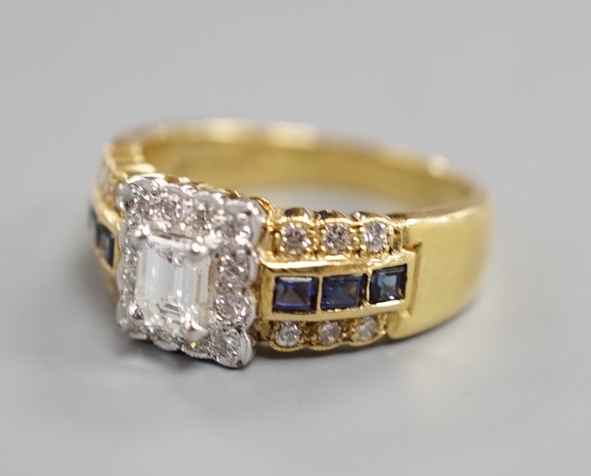 A modern 18ct gold, emerald and round cut diamond set square cluster ring, three three row sapphire and diamond set shoulders, size M, gross weight 6.6 grams.